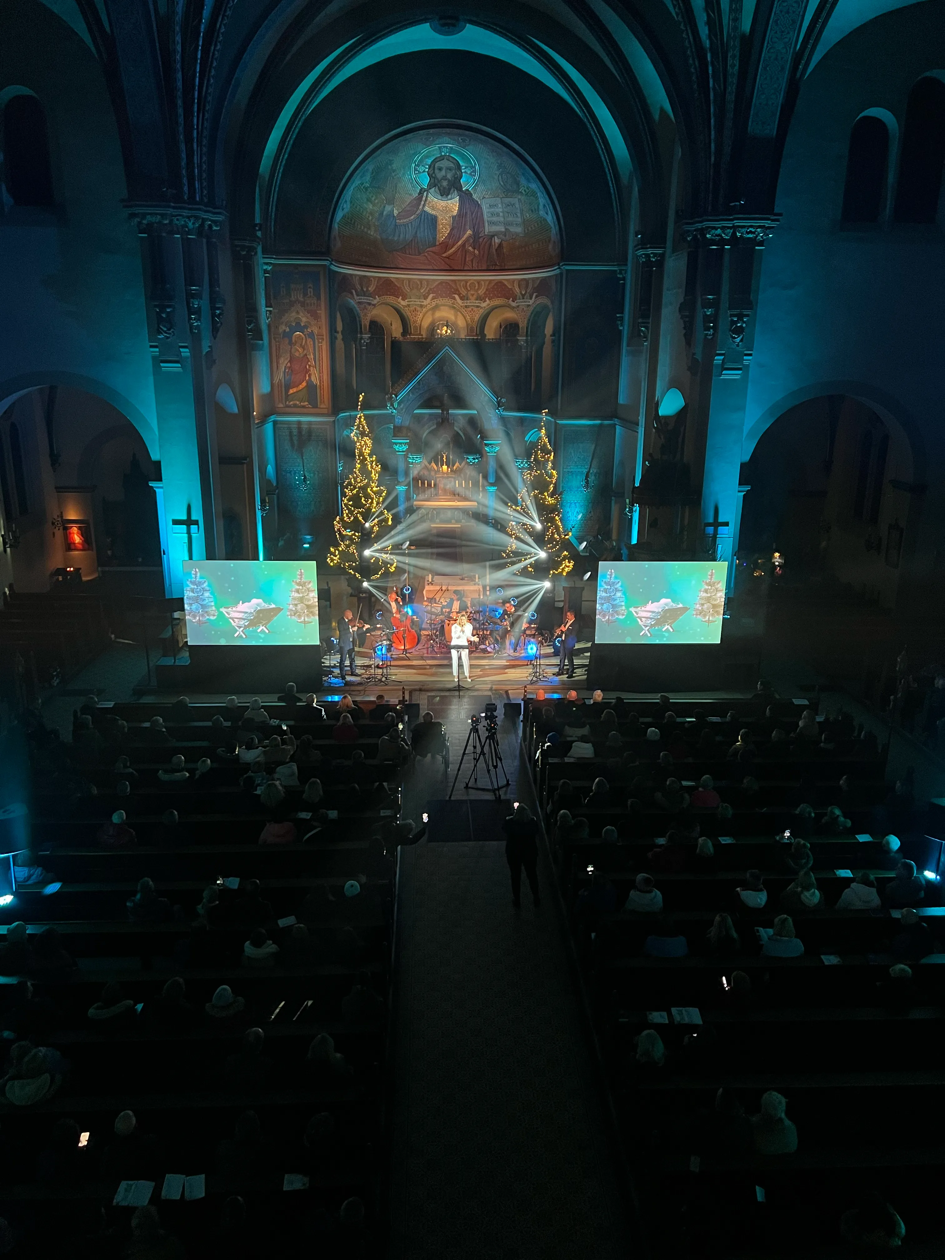 Concert stage with a band and projections inside a tall historic sacred interior.